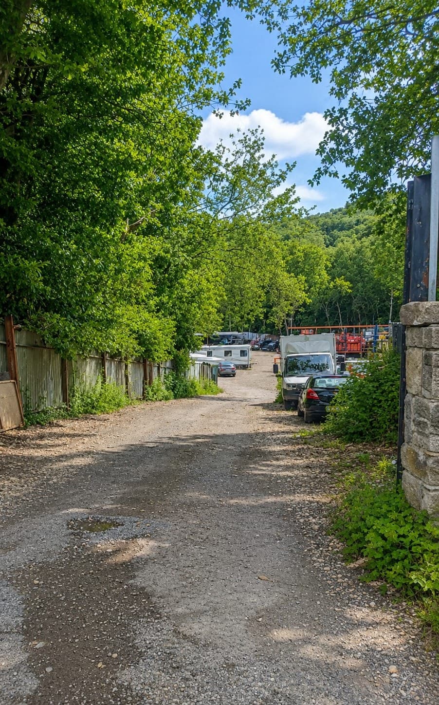 The gravel track into Bargate Yard, running between a fence and the stone gatepost with vehicles parked along the far side