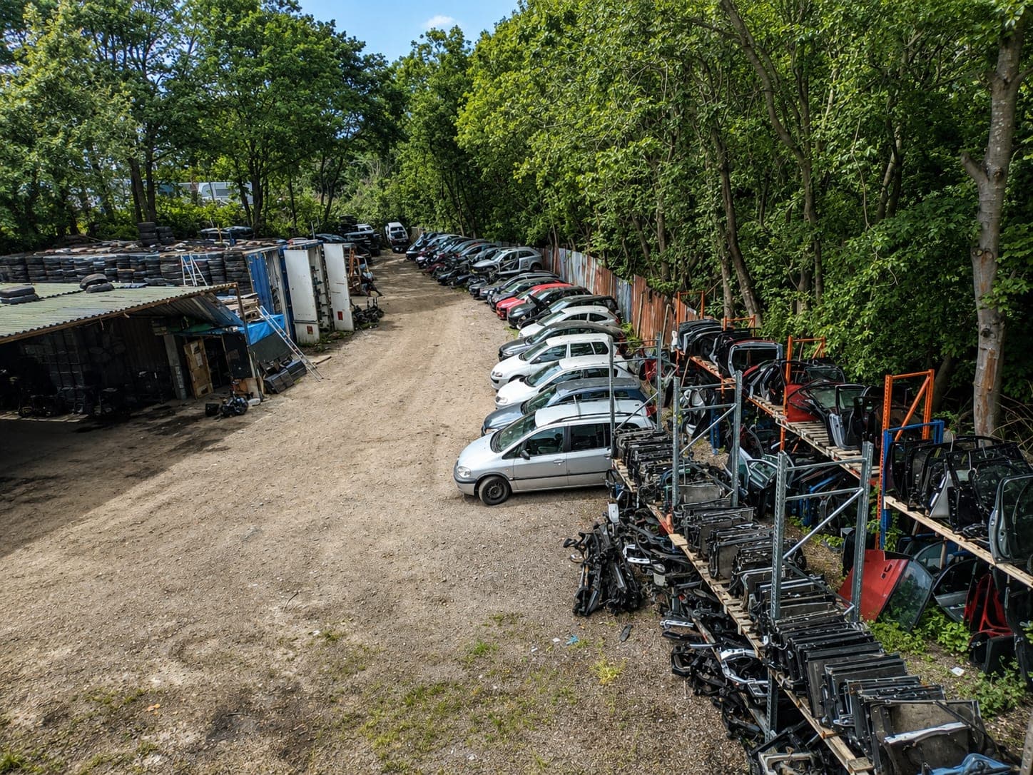 Cars lined up along one side of the yard waiting to be stripped, with racking of recovered doors and panels beside them